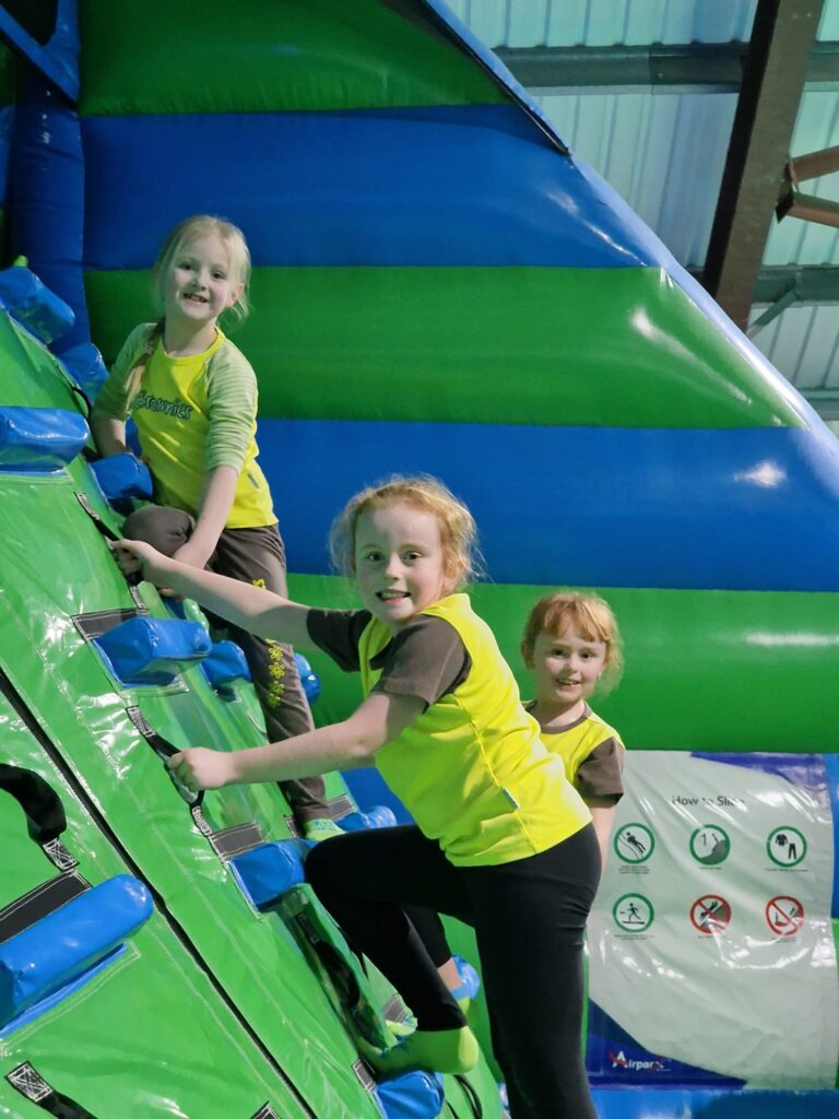 Three Brownies climb an inflatable while smiling