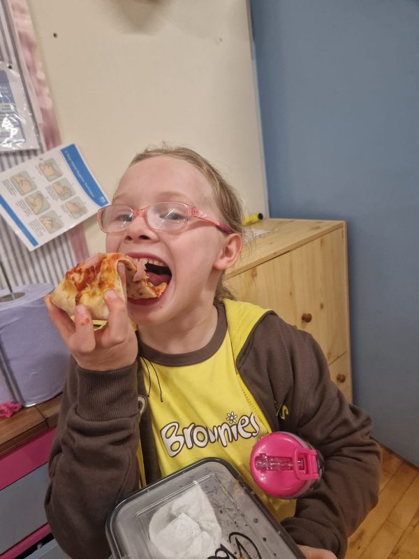 A Brownie smiles while eating her pizza