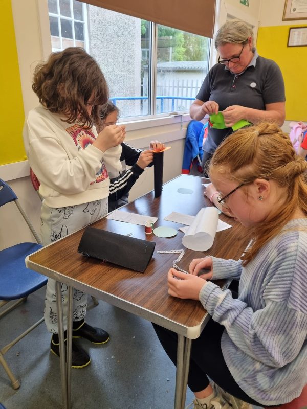 A group of girls stand around a table doing a craft