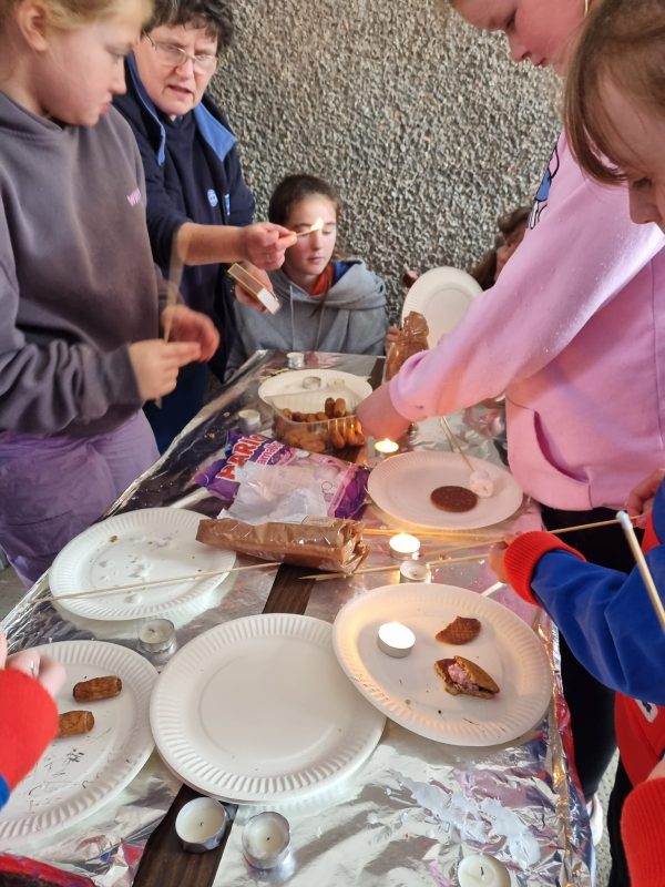 Girls and a leader stand outside around a table preparing smores